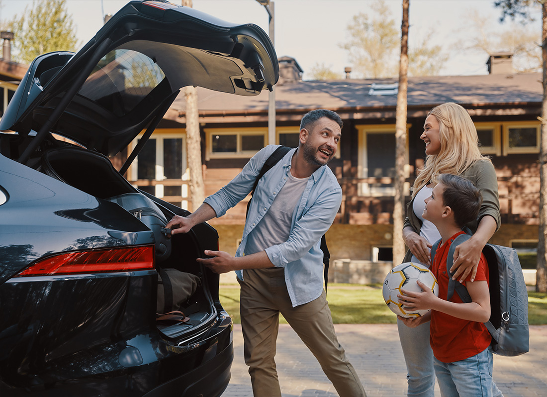 Personal Insurance - Happy Young Family Packing Stuff Into the Car and Smiling While Standing Near a House